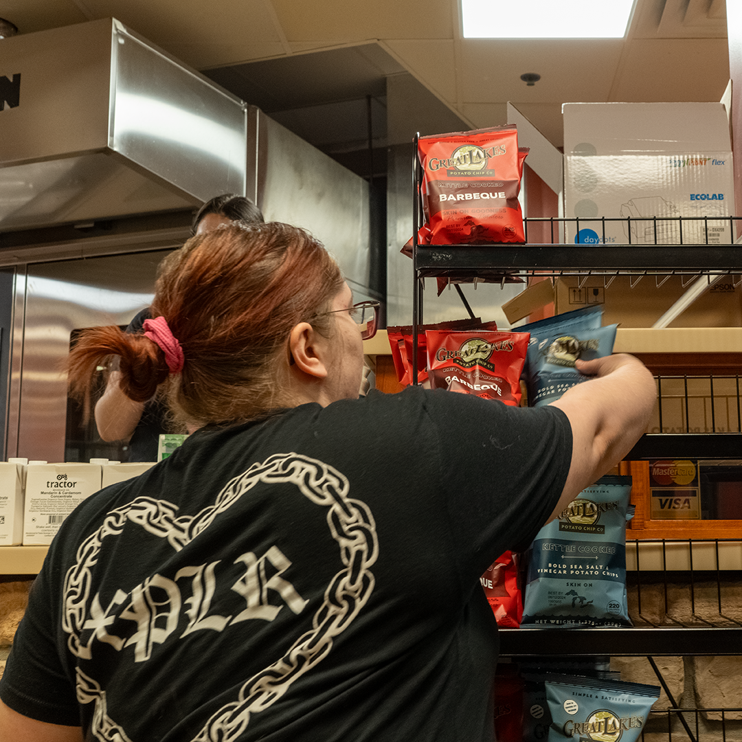 "A member of the Parkhurst Staff adding new "Great Lakes" brand potato chip bags to a display in the new Rock Creek Cafe and Bakery"
