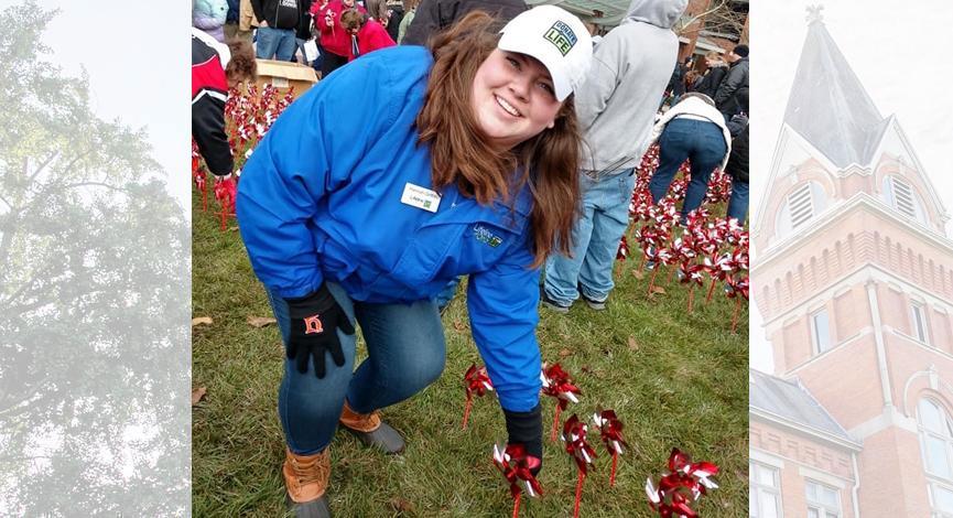 Hannah Griffith, in blue jacket and white hat, reaches down to ground to plant pinwheel