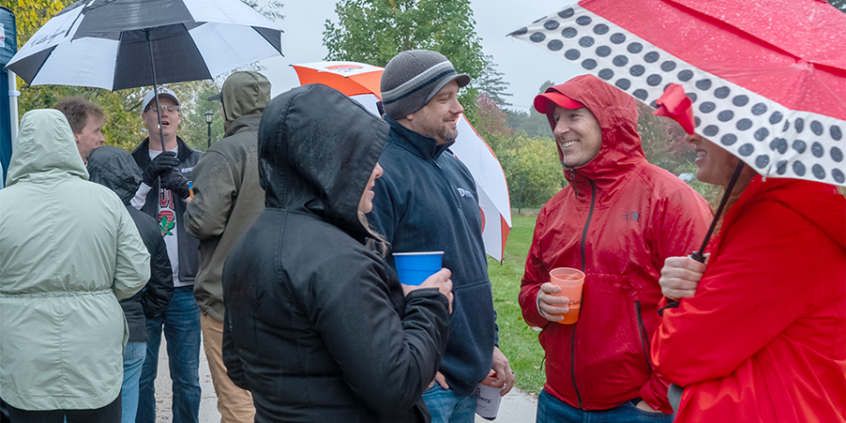 Alumni gather and reconnect holding umbrellas on Saturday