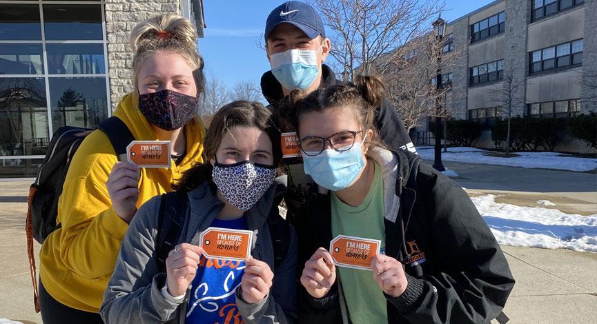 Four students, wearing masks, posing for a photo with their TAG Day stickers