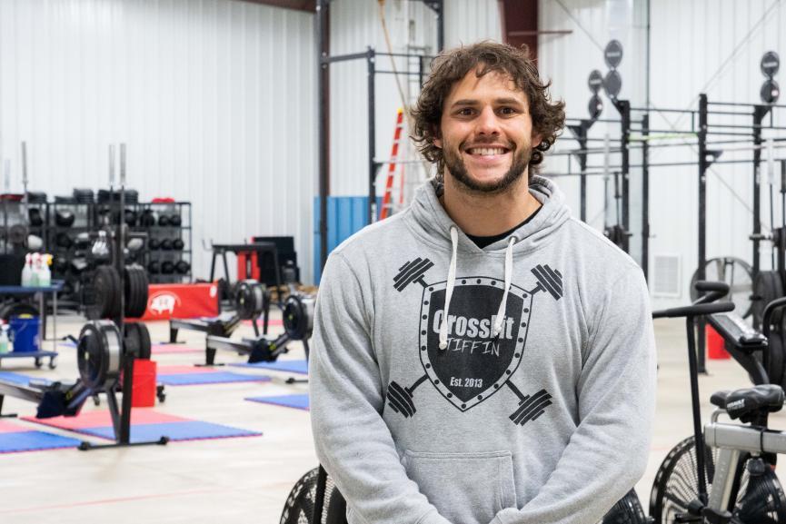 Jared Poses for photo in sweatshirt standing in the forefront of the interior of the gym