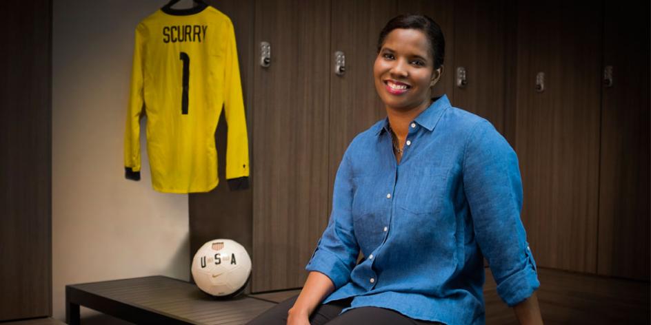 Brianna Scurry sitting on bench with soccer ball and jersey in the background