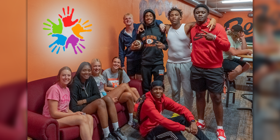 A group of several diverse students hanging out in the Brown basement lounge. The walls are orange and an image of 5 multicolor hands is superimposed.