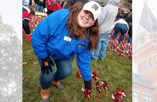 Hannah Griffith, in blue jacket and white hat, reaches down to ground to plant pinwheel