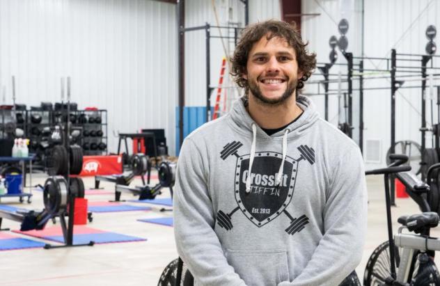 Jared Poses for photo in sweatshirt standing in the forefront of the interior of the gym