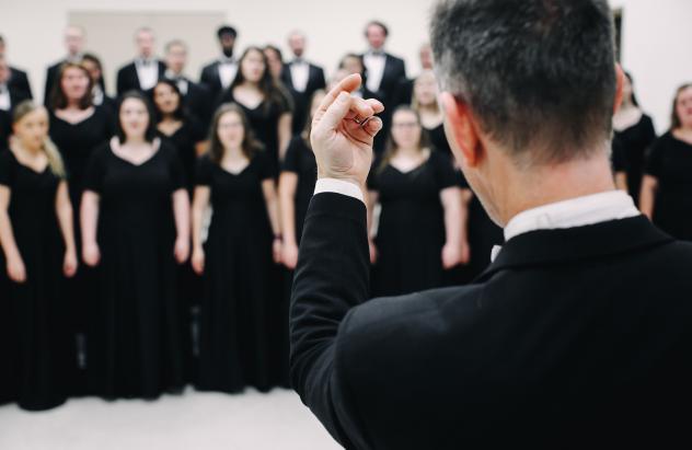 Concert Choir director conducts with the choir in the background out of focus
